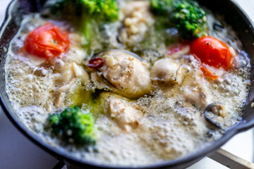 レストランやバルで提供される、熱々のオイルで煮込まれた大粒の牡蠣とブロッコリーの彩り豊かなアヒージョ。シズル感あふれる調理シーン