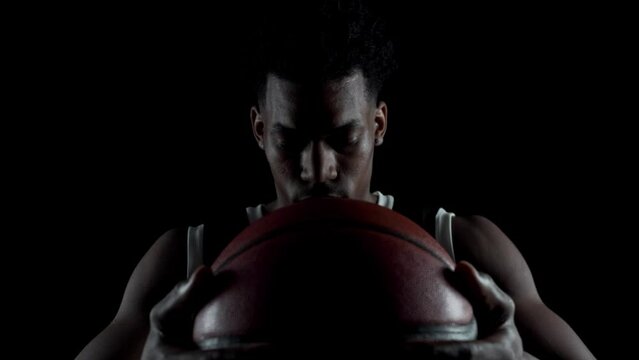 Basketball player sitting on a bench taking deep breath in. Concentrated african american sports man against black background.