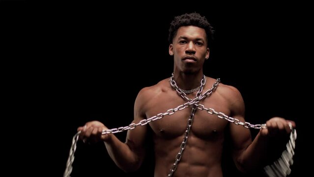 Muscular man showing muscles and spinning a chain. African American male posing against black background.