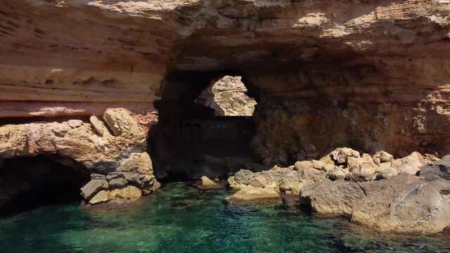 secret cave hole in mountain at bay.Unbelievable aerial view flight fly backwards drone footage of cliff edge beach Sa Figuera borda Ibiza summer 2022