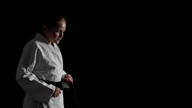 Young karate girl wearing kimono and dancing against black background