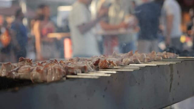 Meat on skewers steaming on sizzling barbecue at public event 
