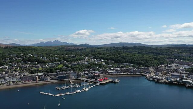 Beautiful drone shot of Oban, Scotland, panning along the whole coast of the town, revealing the sea and mountains all around.