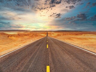 Endless highway road with dramatic sunset clouds on the horizon desert landscape.