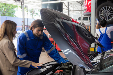 Young man mechanic talking with customer for examining trouble and repairing engine of car in the garage, vehicle of asian woman with problem and maintenance, advice of technician about automobile.