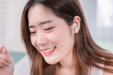 Asian woman use smartphone and wearing earbuds listening music entertainment her enjoy and fun sitting on sofa in living room at home