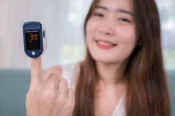 Asian woman using finger oxygen meter on sofa in living room at home, health and living concept
