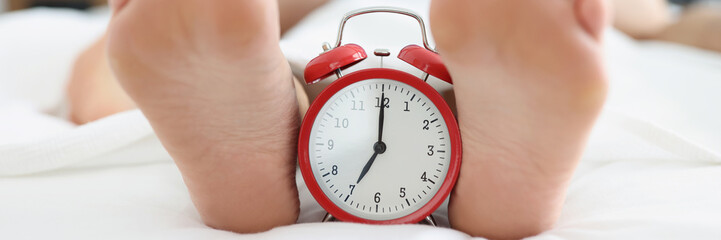 Red alarm clock for seven in morning or evening on bed of sleeping people.