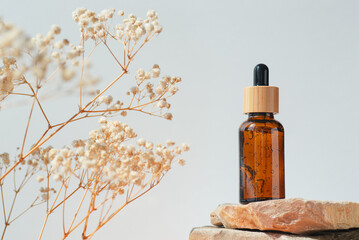 Amber dropper bottle with serum or gel on stone podium. White background with yellow flowers....