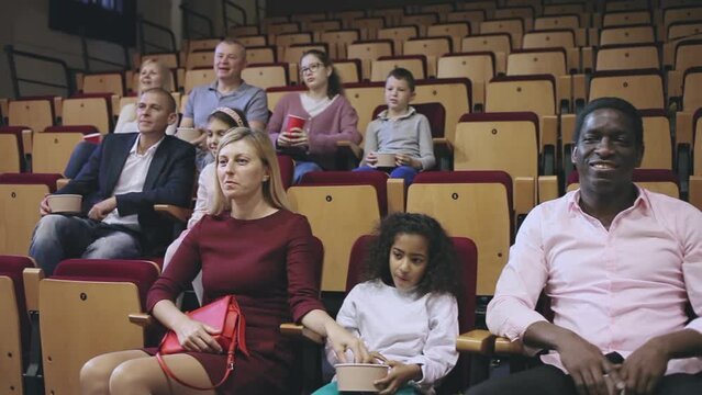 Interested adults with tween children absorbedly watching film in movie theater. Concept of joint leisure of parents and children. High quality FullHD footage