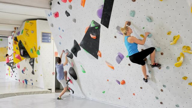 Visitors of bouldering centre, women and man, climbing on wall.