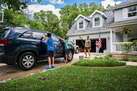 Air Force service member washes his vehicles with his sons in the driveway.