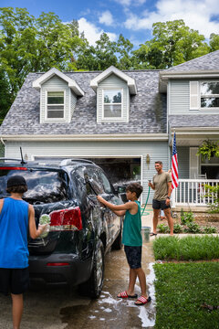 Air Force service member washes his vehicles with his sons in the driveway.