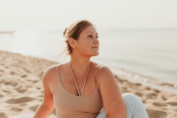 Fototapeta na wymiar Caucasian woman practicing yoga at seashore sandy beach on sunrise. Womens health and wellness. Sports body positive. Real instructor poses