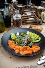 salmon with avocado and greens in a black plate
