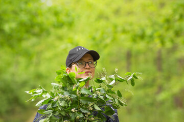 Young caucasian woman in black cap and glasses holds a green bunch of bird-cherry twigs. Nature green background.