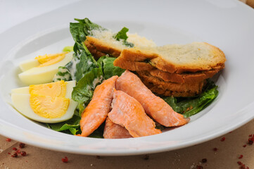 caesar salad with salmon in a traditional serving in a white plate, macro photo
