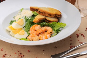 caesar salad with shrimp in a traditional serving in a white plate, macro photo
