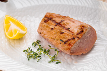 fried tuna fillet in a white plate with lemon and thyme
