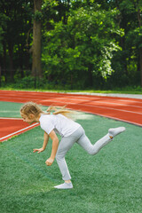 A little girl goes in for sports on the grass, the child does a warm-up before training at the stadium. Children's sports and healthy lifestyle.