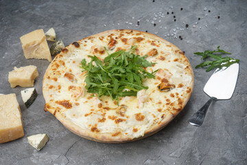 pizza with shrimps mussels and arugula on a gray background with cheese and a spatula
