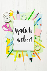 Children's accessories for study, creativity and office supplies on a white wooden background. Handwritten inscription Back to school on a white notebook.