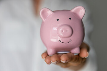 female hands puts a coin in a pink piggy bank. The concept of saving money or savings, investment