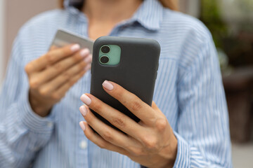 female hands hold a modern mobile phone and a bank credit or debit card on the street..ordering purchases, working online, transferring money by phone
