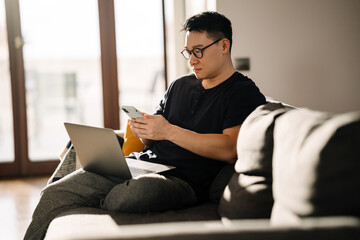 Adult calm asian man sitting on sofa with laptop