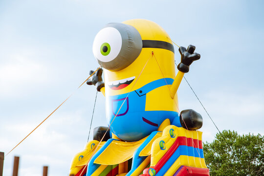 Huge inflatable figure one-eyed yellow minion. Inflatable children's attraction trampoline in a public park.