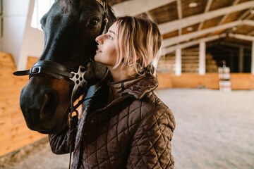 Young blonde jockey woman spending time with her horse