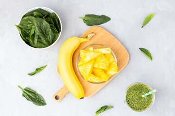 Vegetarian green smoothie with avocado, spinach leaves, pineapple and banana in glass on gray...