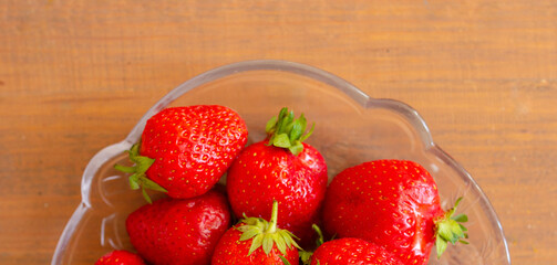 Many red strawberries on glass plate and wooden table top view banner