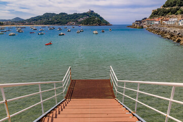 Fototapeta na wymiar Steps leading into the water in La Concha bay with boats with Santa Clara island in the background, San Sebastian or Donostia in Basque Country, Spain