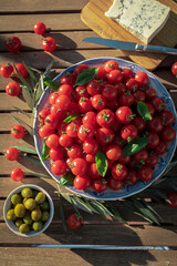 Wooden table in the garden with cherry tomatoes, olives and platter with gorgonzola cheese. Healthy snack in the garden