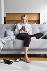 Woman sits on couch with smartphone