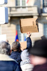 Rear view of senior man holding blank placard carton piece protesting in front of the building -...