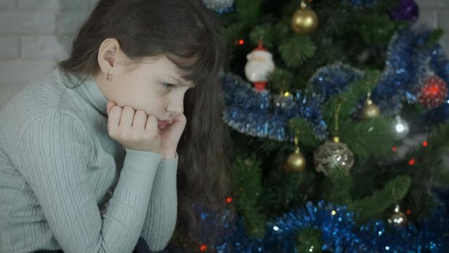 Offended child at Christmas. An offended girl sits in loneliness by the Christmas tree in the room.