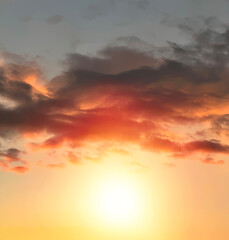 Dramatic sunset landscape with puffy clouds lit by orange setting sun and blue sky.