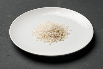Heap of dry rice in a bowl on black background, lack of food, hunger concept