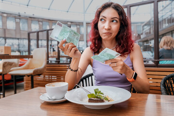 A frustrated girl pays for her dessert in a coffee shop with a euro bill. The concept of inflation and a sharp increase in prices