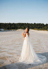 Fototapeta na wymiar Beautiful girl in wedding dress posing in front of desert, sand, canyon with a bouquet in her hands