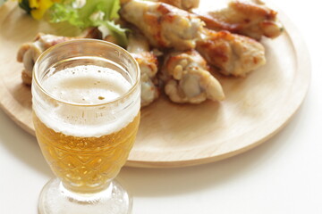 Barbecue chicken drumsticks on wooden plate and glass of beer