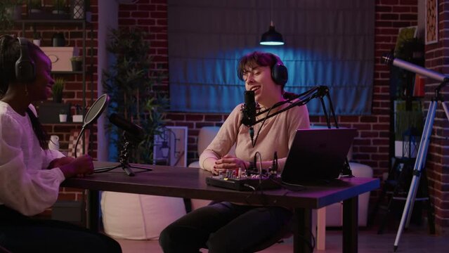 Online radio host doing high five hand gesture with african american guest singer in living room home studio. Two women with headphones high fiving during internet talkshow while recording podcast.