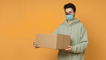 male delivery man in two protective masks holding a cardboard box, colored background with copy space