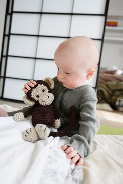 Cute baby boy playing with toy monkey at home
