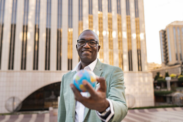 Happy mature businessman with globe figurine standing in front of building