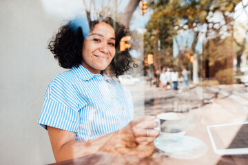 Smiling woman with coffee cup seen through glass of cafe