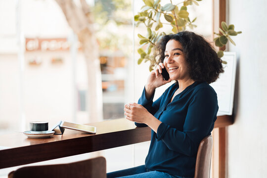 Cheerful woman talking on mobile phone at table in cafe