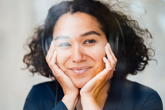 Smiling woman listening music through headphones seen through glass